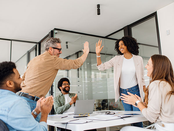 Associates sharing a moment of success with high-fives and applause around an office table